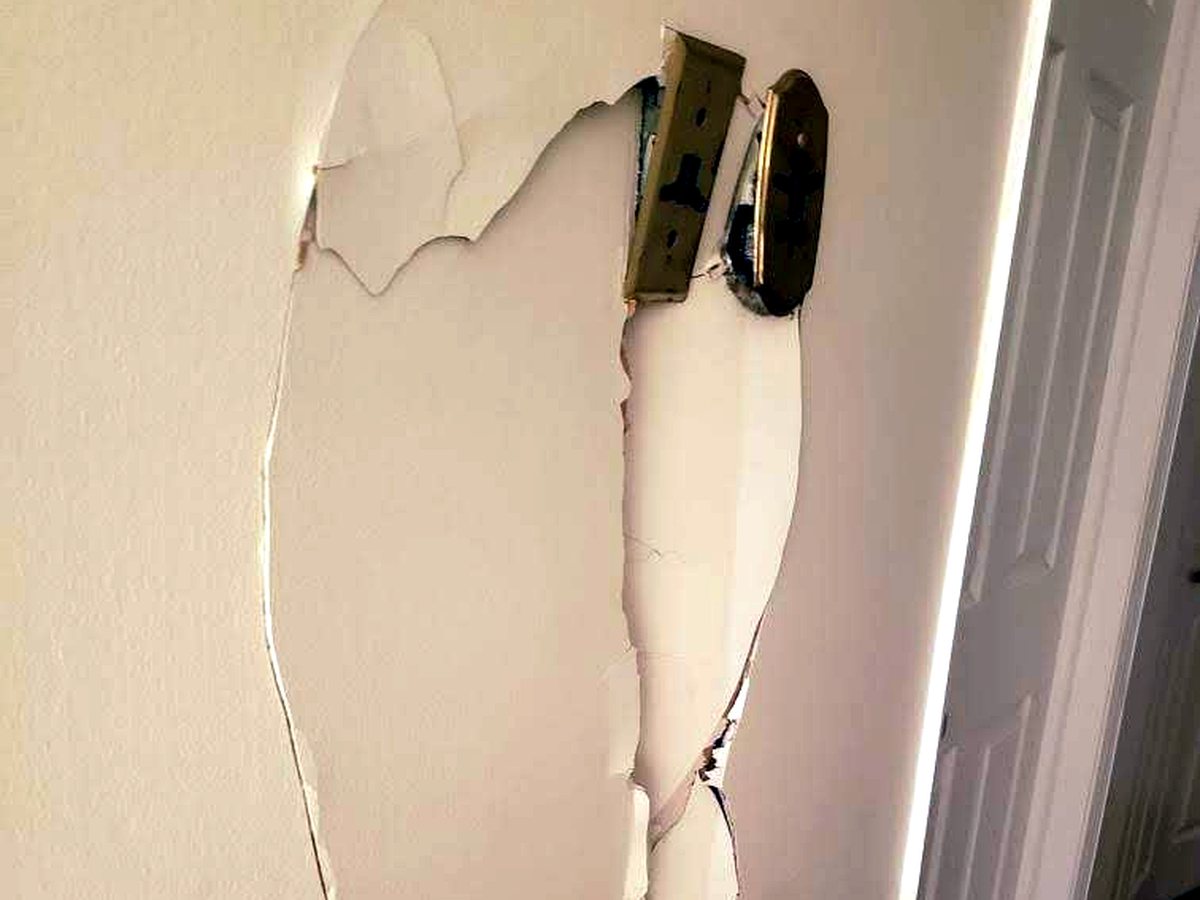 Damaged drywall with exposed electrical box and torn wall surface